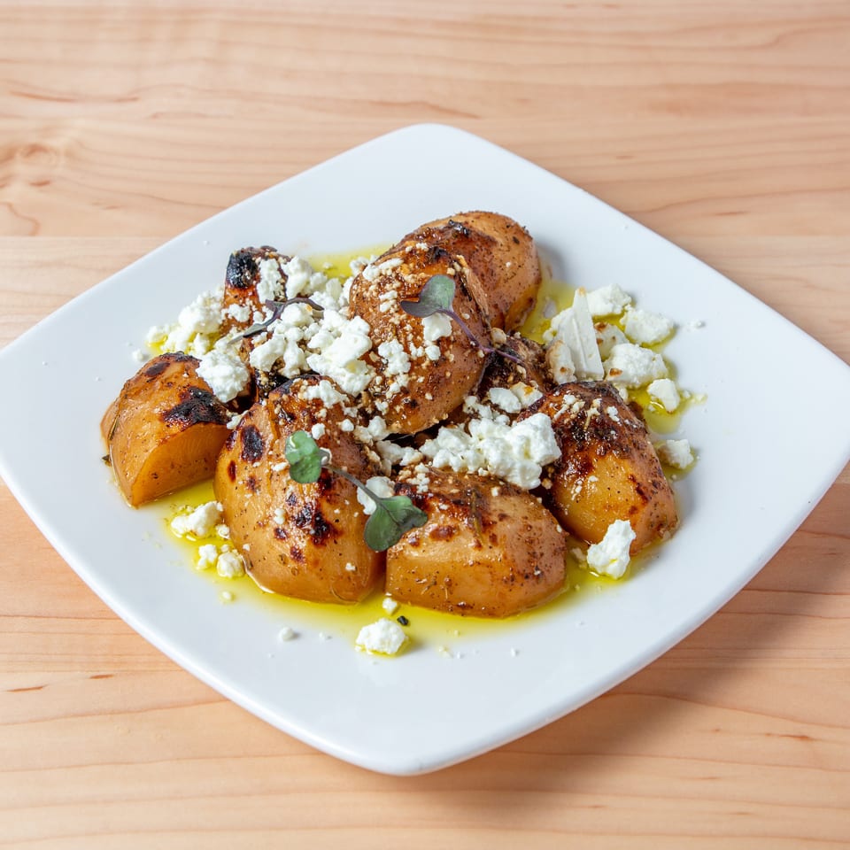 Roasted potatoes topped with crumbled feta cheese, herbs, and olive oil on a white plate.