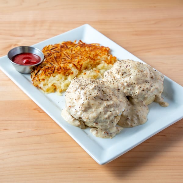 Biscuits and gravy with hash browns and a side of ketchup on a white rectangular plate.