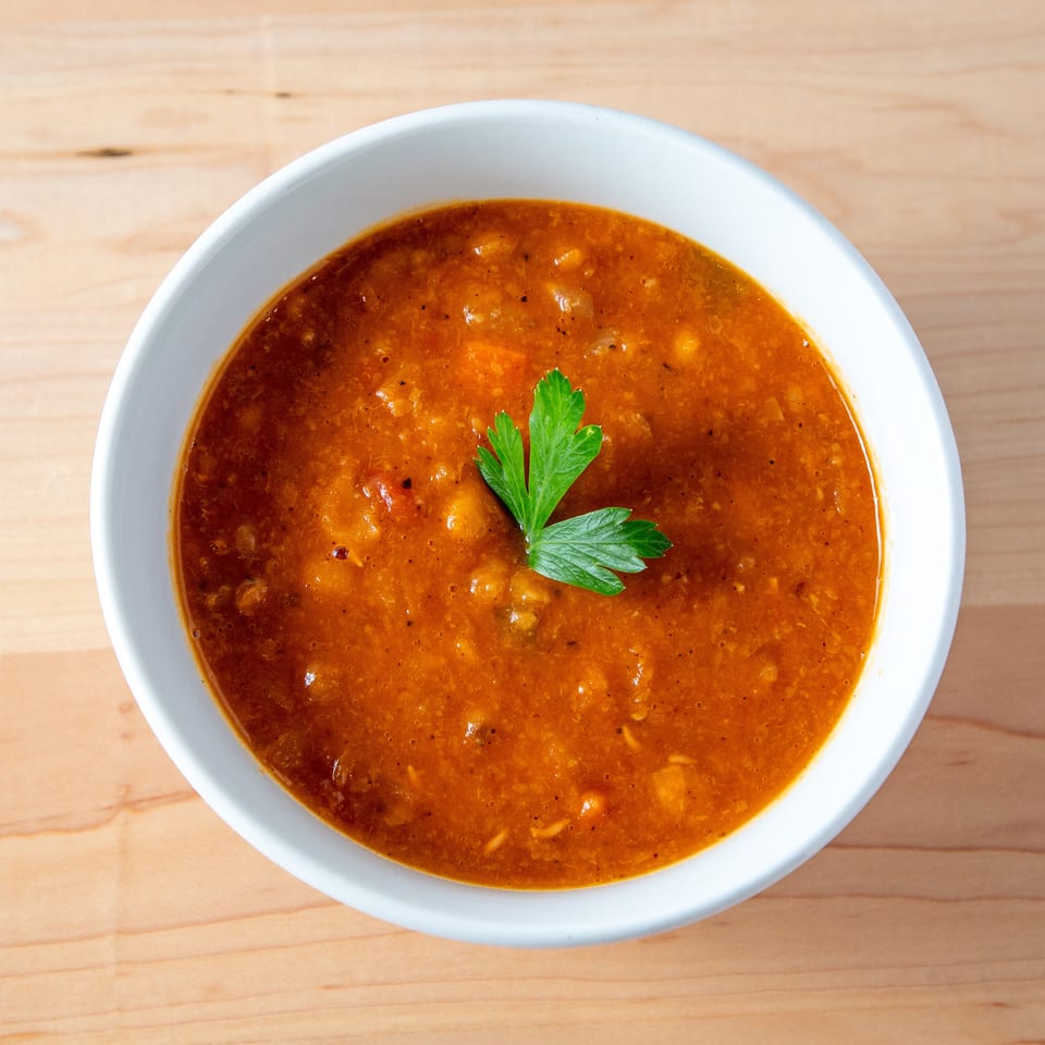 Hearty lentil soup in a white bowl, garnished with fresh parsley on a wooden table.