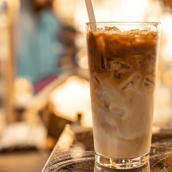 Tall glass of iced coffee with milk swirls and a straw on a reflective surface.