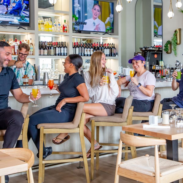 Diverse group of happy people enjoying drinks and conversation at a lively bar with TVs in the background.