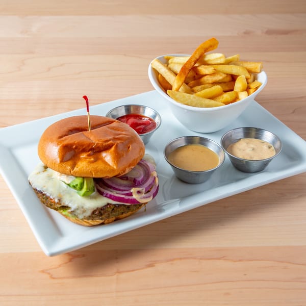 A burger with cheese, avocado, and red onion, served with fries and dipping sauces on a white plate.