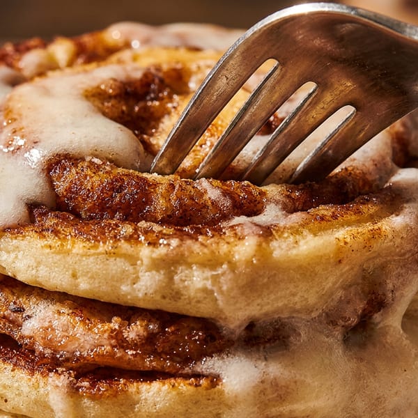 Fork in a stack of cinnamon rolls with sweet white icing.