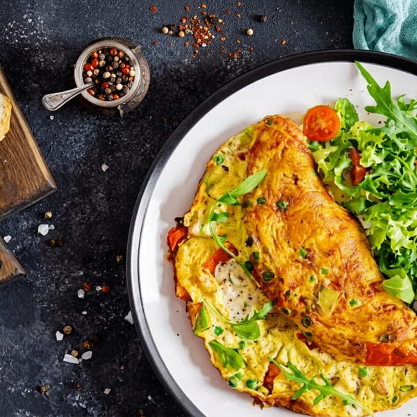 A fluffy omelet with vegetables, a fresh green salad, and crusty bread slices.