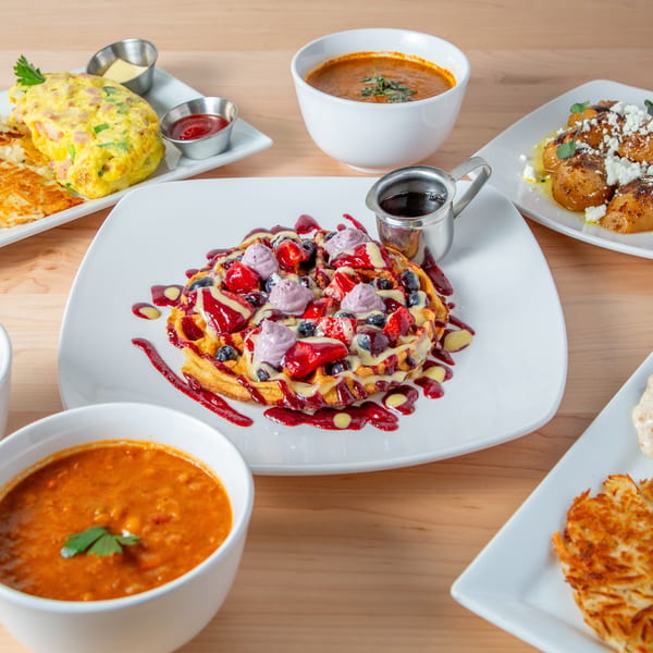 A table filled with various breakfast and brunch dishes, including waffles, omelets, and soups.