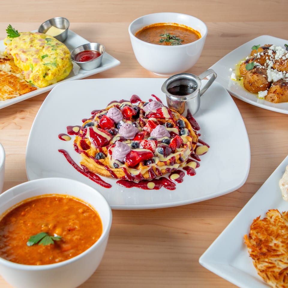 A table filled with various breakfast and brunch dishes, including waffles, omelets, and soups.