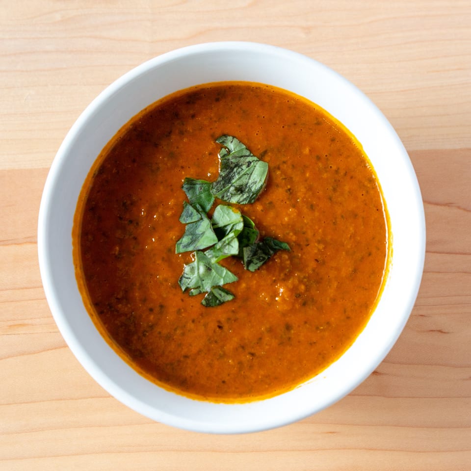 Overhead view of a white bowl filled with orange tomato soup, garnished with fresh basil leaves.